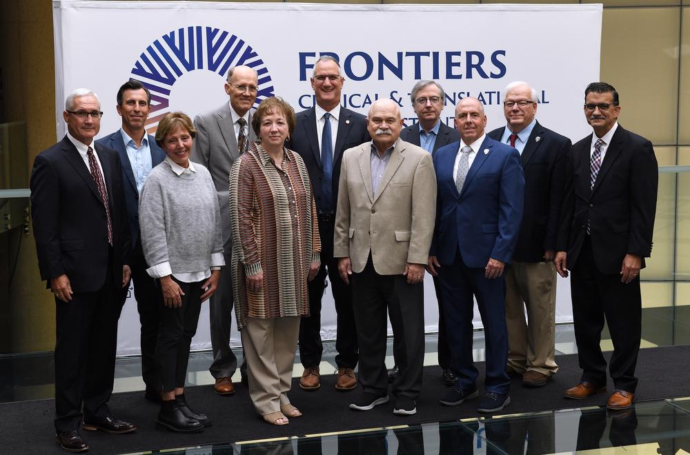 Two women and 9 men in front of a sign
