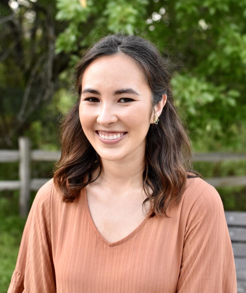 smiling woman wearing pink shirt in front of a fence and trees
