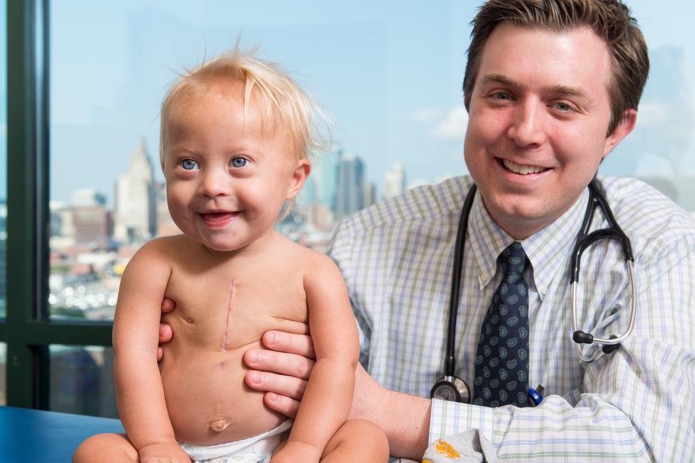 smiling man in checked shirt and stethoscope holding a small child