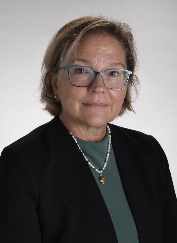 woman with glasses smiling wearing green shirt with black jacket and a necklace