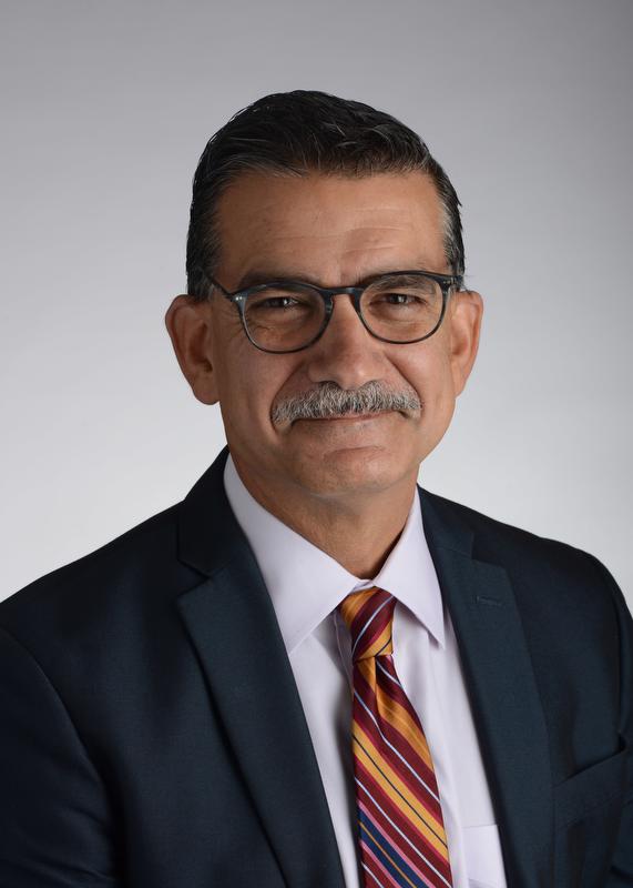 Image of Mario Castro M.DMario Castro wearing black jacket, white shirt, multi-colored tie and cglasses, smiling at camera.