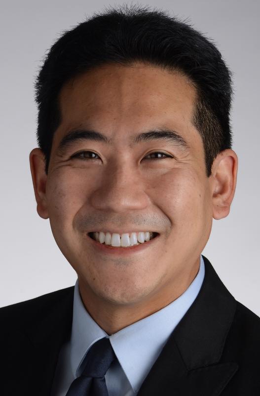 Image of Hanluen Kuo wearing a black jacket, blue shirt, and tie