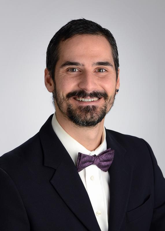 smiling man in black jacket, white shirt and purple bow tie