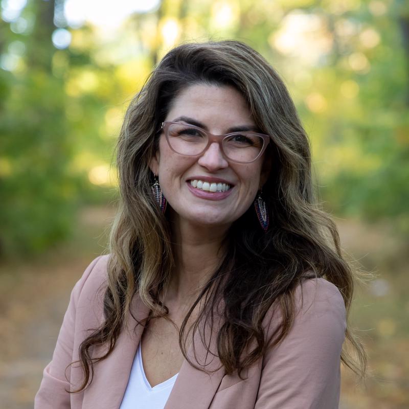 smiling woman with tree backdrop wearing white shirt and pink jacket