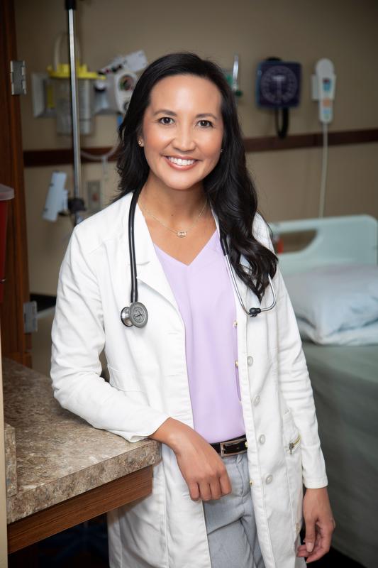 smiling woman in purple shirt wearing white jacket with stethoscope