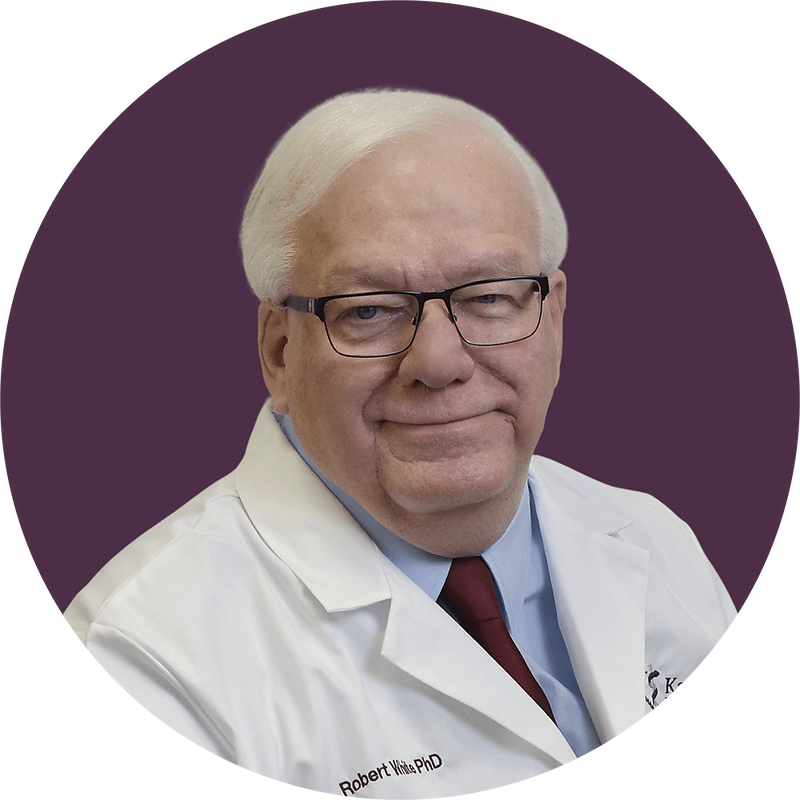 man in white doctor coat, wearing blue shirt and purple tie with a purple background in the back