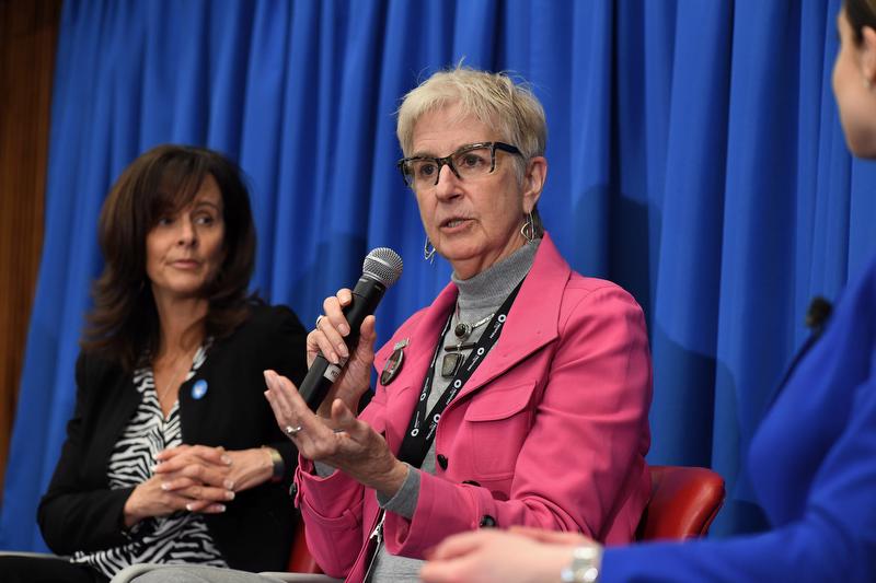 woman in pink blazer holding a microphone with a woman in a black jacket next to her
