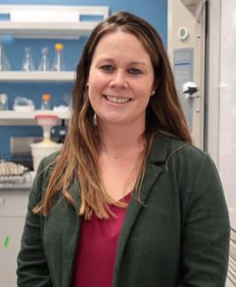 smiling woman in a lab wearing a green jacket and pink shirt