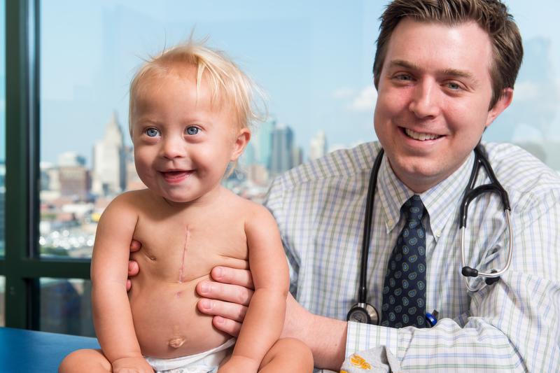 smiling man in checked shirt and stethoscope holding a small child
