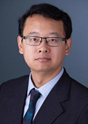 man wearing glasses and black jacket, blue shirt and red and blue patterned tie