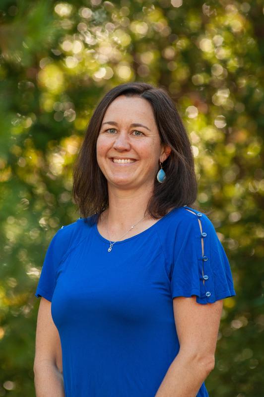 smiling woman in blue shirt and earrings with trees in the background
