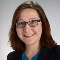 smiling woman wearing black jacket and blue shirt, and glasses