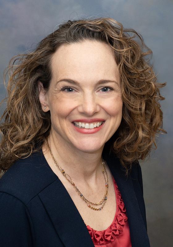 woman smiling wearing a black jacket, red shirt and gold necklace