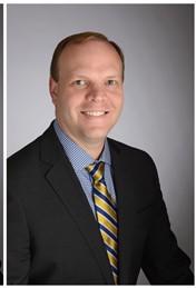 smiling man wearing a black jacket, blue shirt and gold and blue tie