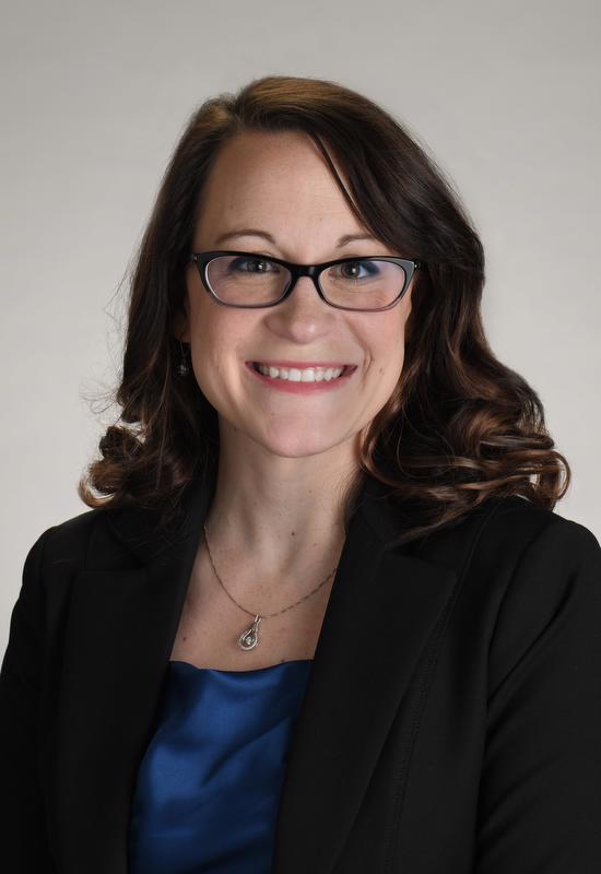smiling woman wearing glasses, black jacket, blue shirt and necklace