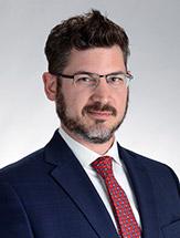 man wearing glasses, blue jacket, white shirt and red and blue tie. he also has a beard