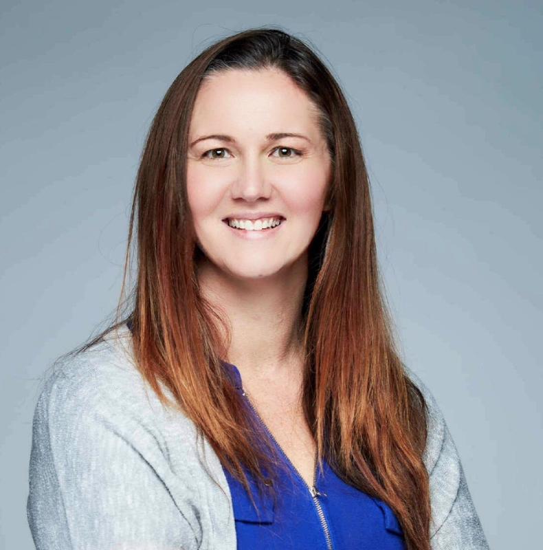 smiling woman with long hair wearing a gray jacket and blue shirt with a zipper