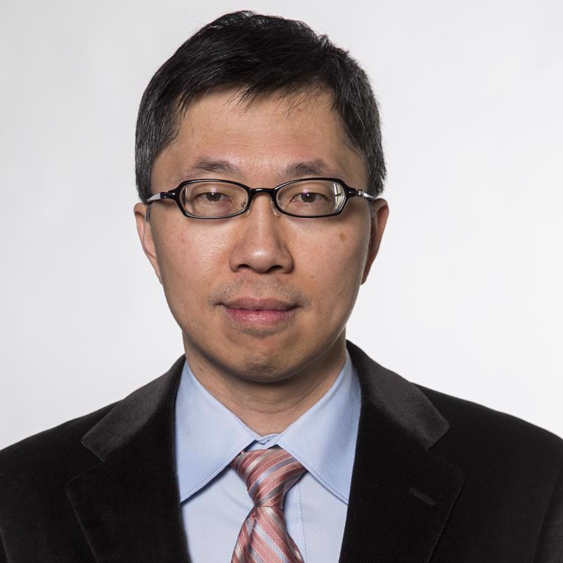 man waring glasses wearing a black jacket, blue shirt and pinkish tie with blue and white stripes