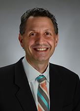smiling man in black jacket, white shirt and blue, white, pink and brown stripped tie