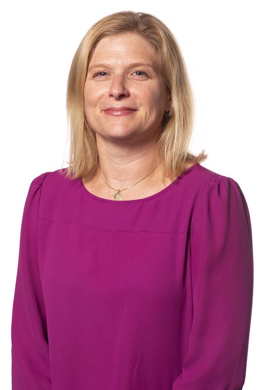 smiling woman with shoulder length hair wearing a purple shirt and a necklace