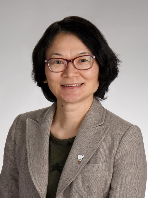smiling woman in glasses wearing a brown shirt with a shuttlecock pin and a black shirt