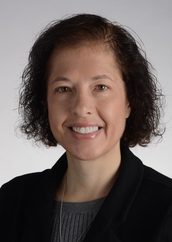 smiling woman with short hair, wearing a black jacket, gray shirt and silver necklace