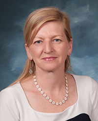 Woman with long hair wearing a white shirt with a black square partially visible. also wearing a necklace