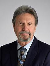 man with a goatee wearing a black jacket, blue shirt and patterned tie