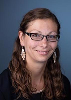 smiling woman with long hair wearing glasses, a black shirt, necklace and long pointy earrings