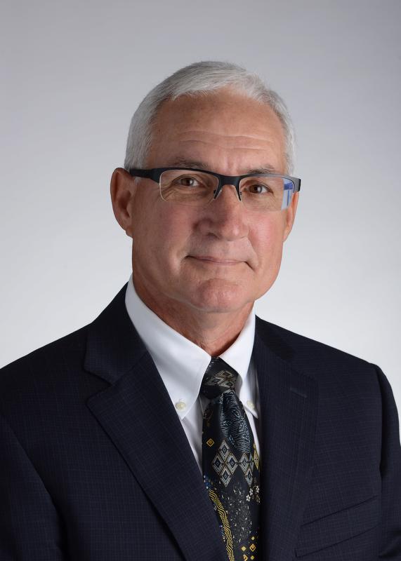 smiling man wearing glasses wearing a black jacket, white shirt and multicolored tie