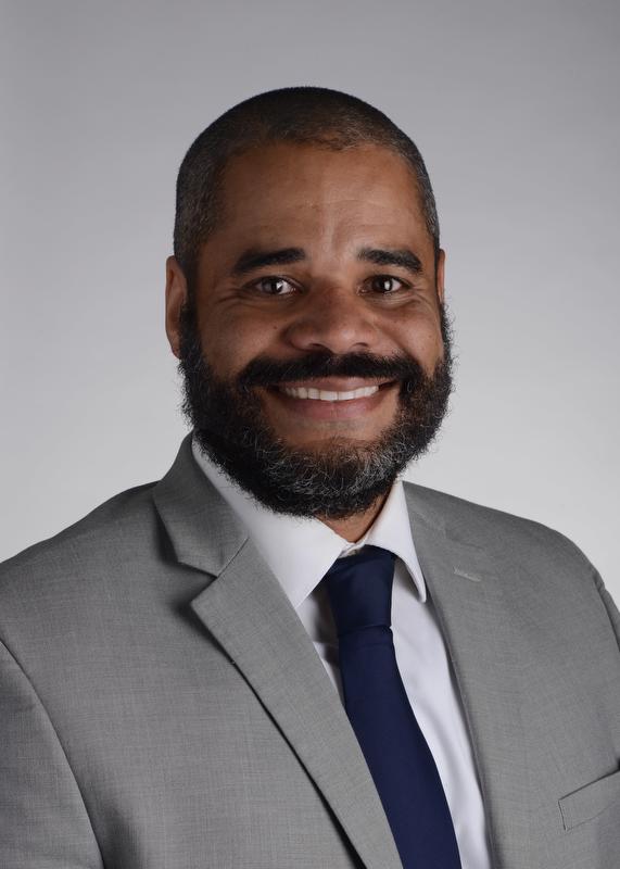 smiling man with beard wearing a gray jacket white shirt and nave blue tie