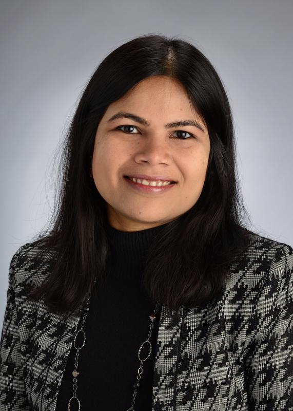 smiling woman with long hair wearing a white and black jacket with designs, black shirt and silver loop necklace