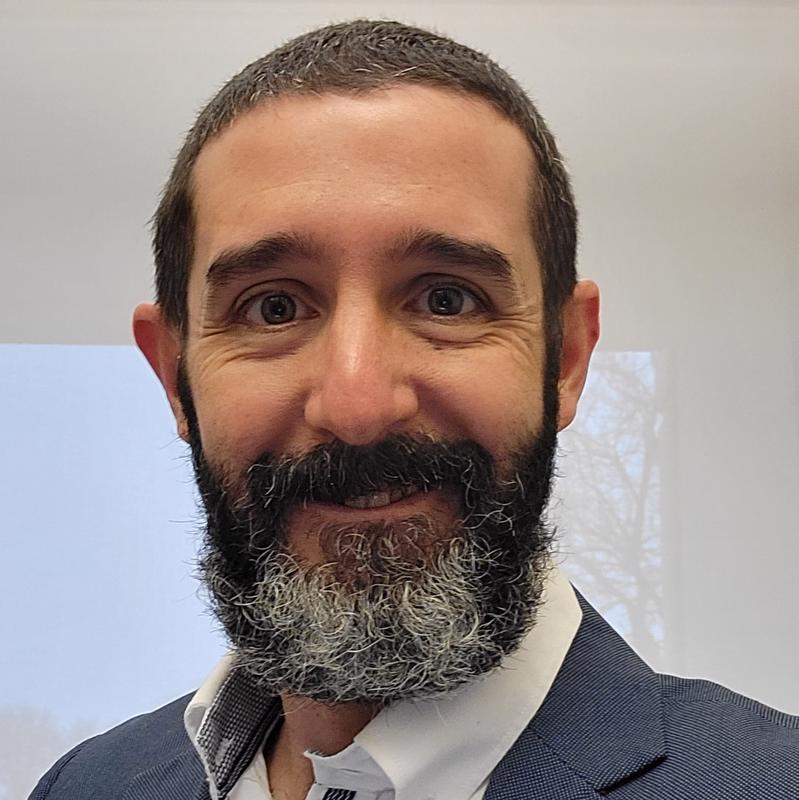 Smiling man with beard wearing a gray suit jacket and white collared shirt