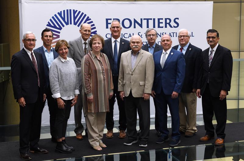 Two lines of people standing in front of a white backdrop. 7 men are in the back line. Two women and two men are in the front line. The men are all wearing ties and the women are wearing slacks with long sleeve shirts