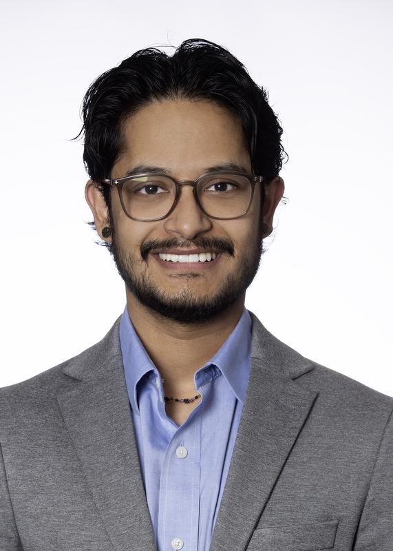 Smiling man wearing glasses, a gray suit jacket and blue button down shirt.