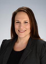 Smiling woman with long hair. She is wearing a black suit jacket and black shirt.