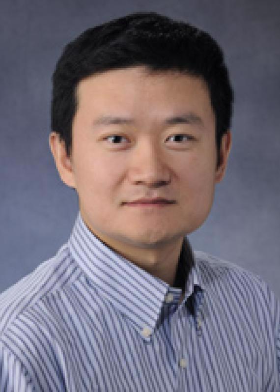 A man with short dark hair wearing a light blue with dark stripes shirt. 