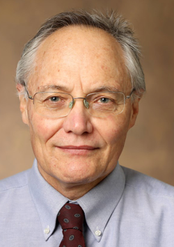 Man wearing glasses, a blue button down shirt and red tie with desgins. Has gray hair.