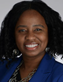 A Smiling woman with shoulder length black hair. She is wearing a blue suit jacket, chunky necklace and black top.
