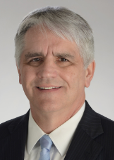 A smiling man wearing a black suit jacket, white shirt and light blue tie.